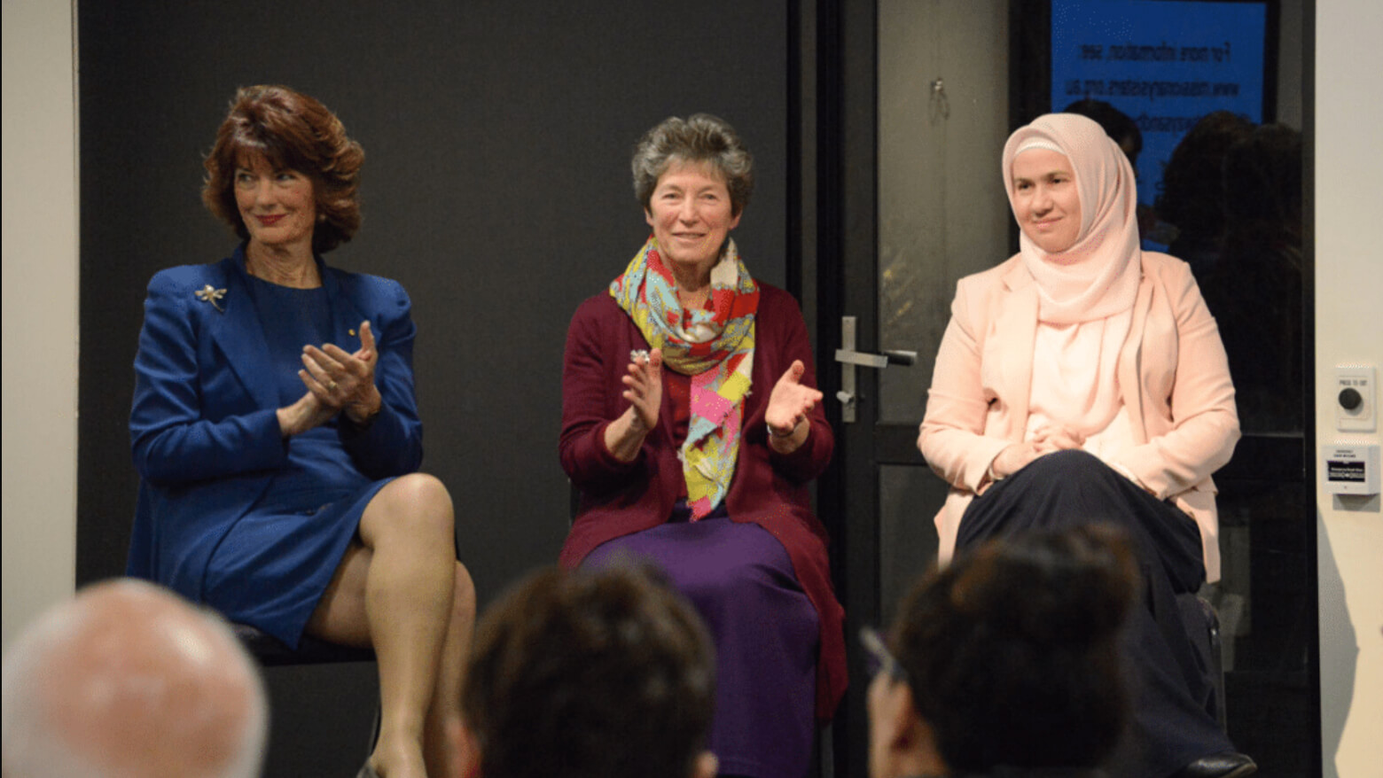 Three women sitting on stage clapping