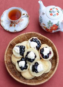 Bowl of scones with cream and jam and pot of tea and cup of tea