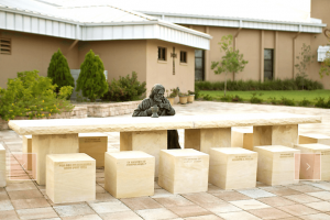 bronze statue of Jesus sitting at table with 12 empty seats