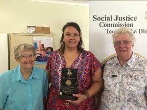 Three women standing, with one holding award