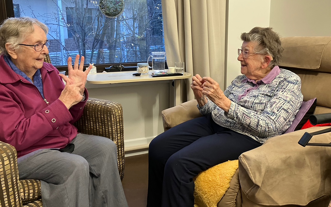 Betty and June Auslan_1080x675 Two women seated facing each other doing AUSLAN