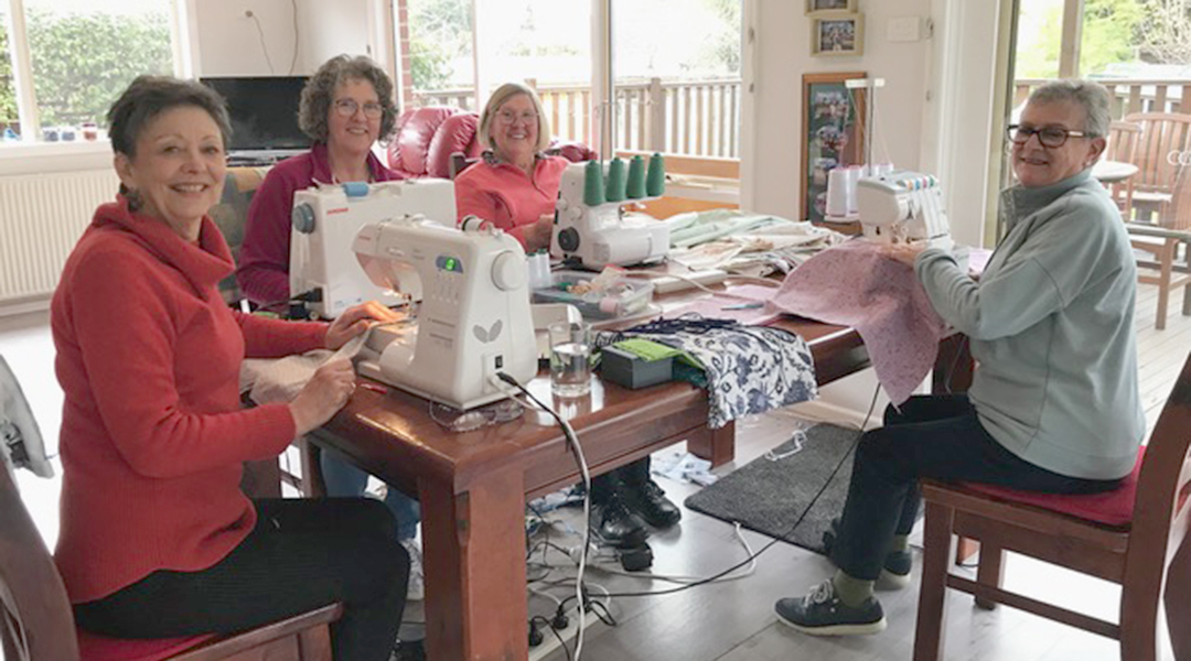 Four women sitting at sewing machines at table